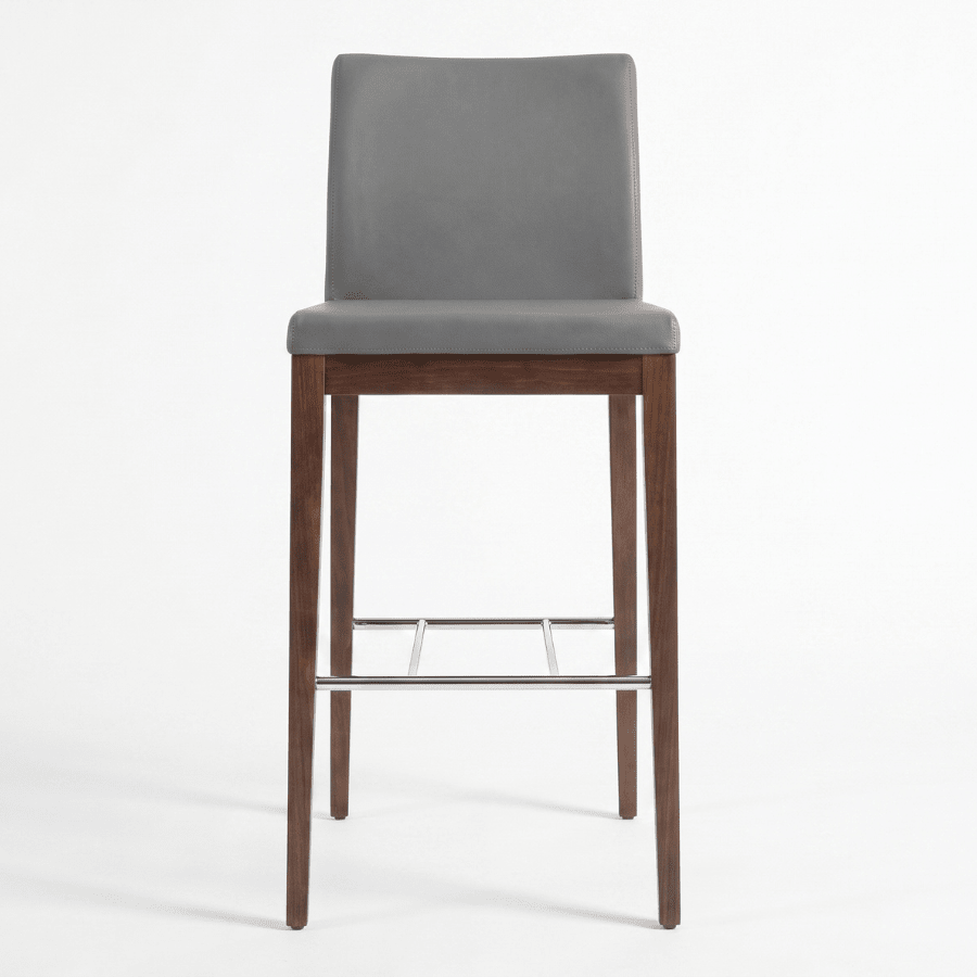 Aria Grey high back bar stool featuring upholstered seat, curved backrest, wooden legs, and chrome footrest