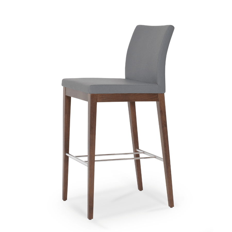 Modern grey high back bar stool with walnut wood legs and chrome footrest against white background